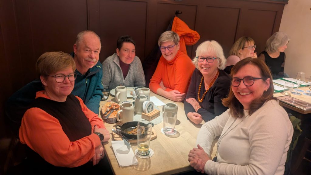 Eine Gruppe Frauen mit einem Mann sitzen um einen Tisch in einem Lokal herum und schauen freundlich in die Kamera